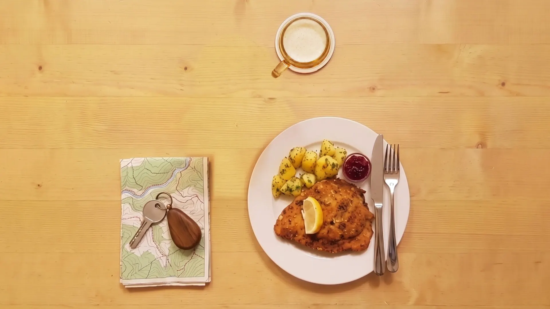Eine gefaltete Wanderkarte und ein moderner Zimmerschlüssel mit Holzanhänger liegen auf dem Holztisch.